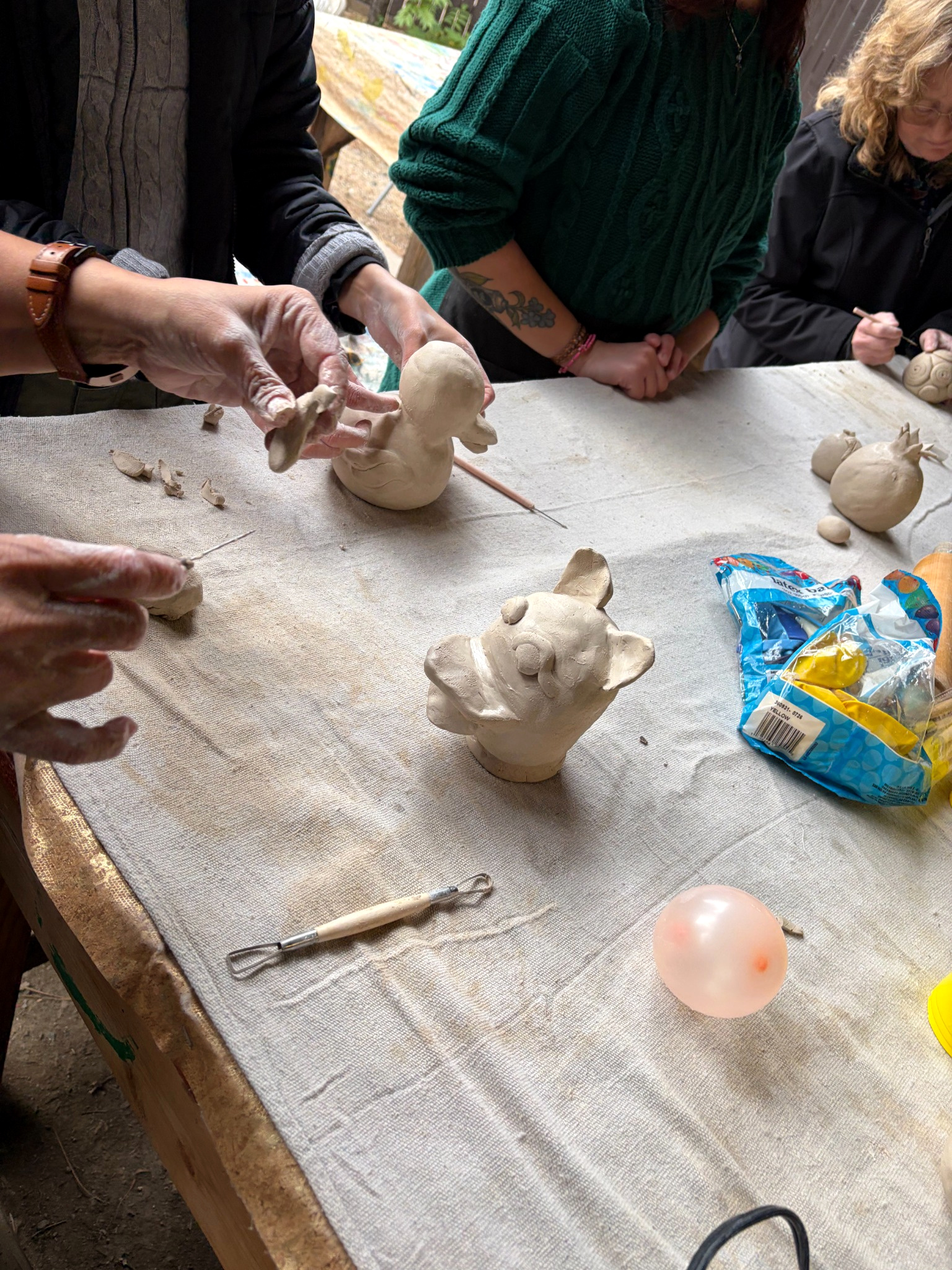 Hands shaping clay as whimsical animal faces take form on a workshop table