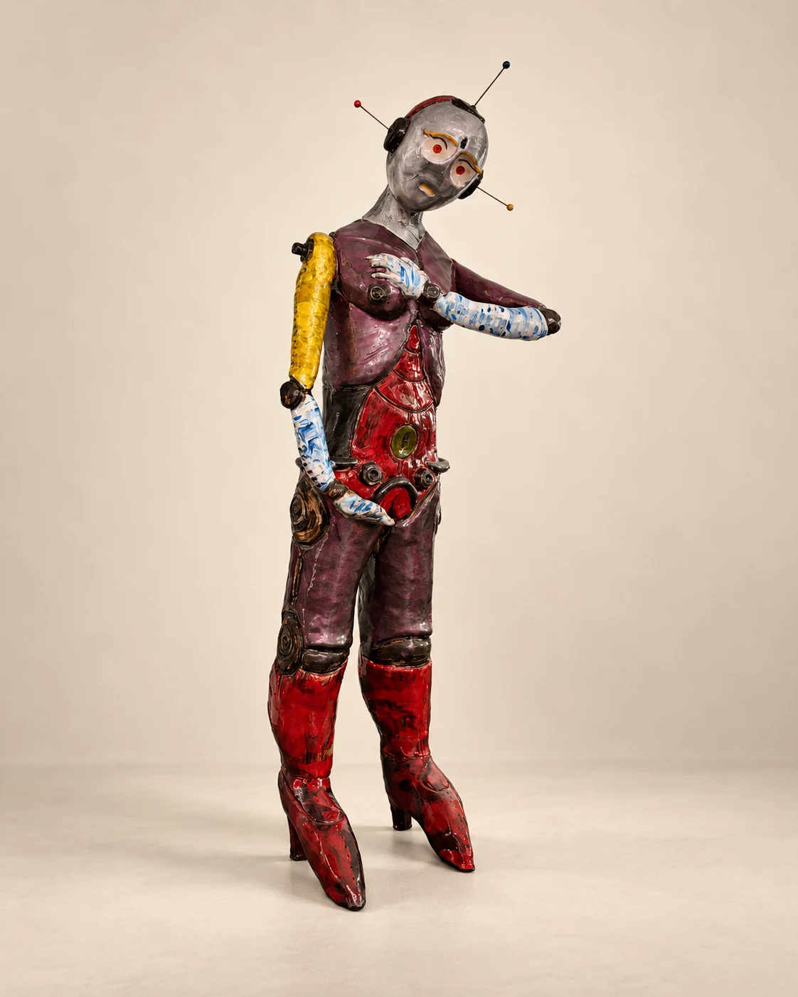 Hand-built humanoid robot sculpture with a silver face, antennae, segmented limbs, and layered red, purple, yellow, blue, and black surfaces